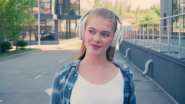 young woman in wireless headphones listening music and walking outside - Footage, Video