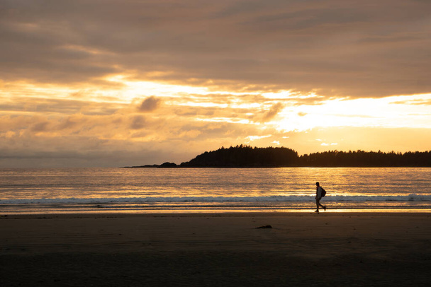A woman walking on the beach under the sunset piercing through the clouds - Photo, Image