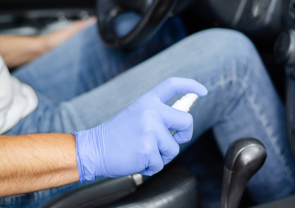 Man sanitizing salon of his car.  Male hand in protective glove holding sanitizer closeup. Disinfection hygiene and coronavirus concept  - 写真・画像