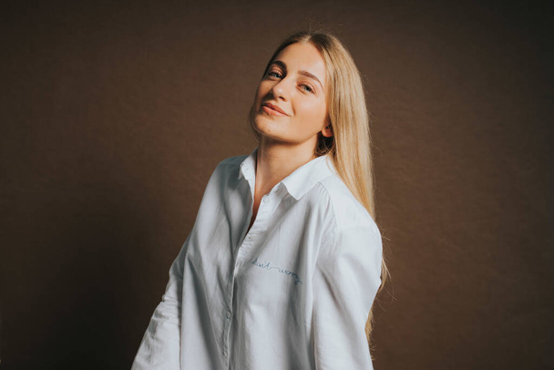 An attractive caucasian blonde female in a white shirt posing on a brown background - Foto, immagini