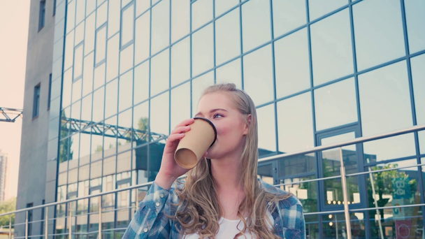 Молодая женщина стоит с рукой в кармане и пьет кофе, чтобы выйти на улицу - Кадры, видео