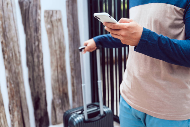 Viaggiatore uomo con valigia tramite smartphone. Prenotazione hotel e volo con smartphone. - Foto, immagini