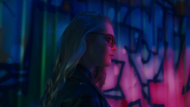 молода жінка в сонцезахисних окулярах, що йдуть біля стіни з графіті
  - Кадри, відео