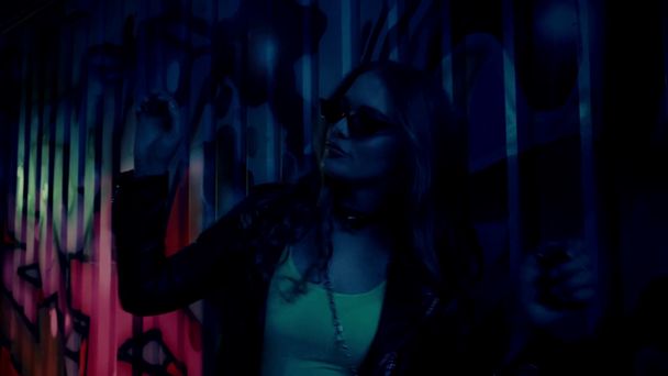 стильная женщина в кожаной куртке танцует у стены с граффити во время вечеринки - Кадры, видео
