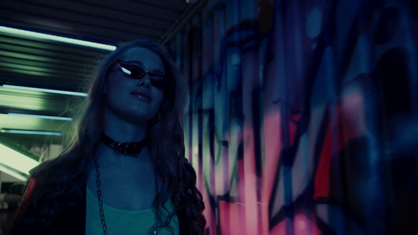 young woman in sunglasses walking near wall with graffiti  - Metraje, vídeo
