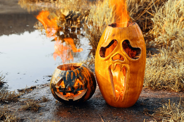 Dos calabazas de Halloween están ardiendo en la orilla del estanque. - Foto, Imagen