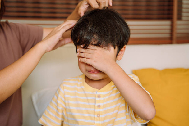 Плачущий азиатский мальчик прикрывает лицо рукой, а мать пытается его вылечить. Травля и депрессия стресс или разочарование. - Фото, изображение