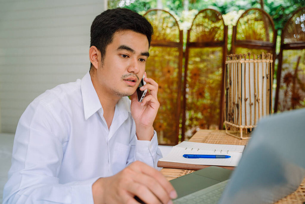 Dospělá asijská recepční v hotelu mluví po telefonu a pomocí notebooku. - Fotografie, Obrázek