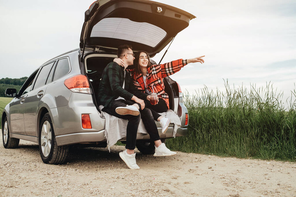 Mladý krásný pár sedí v kufru auta a těší výlet - Fotografie, Obrázek