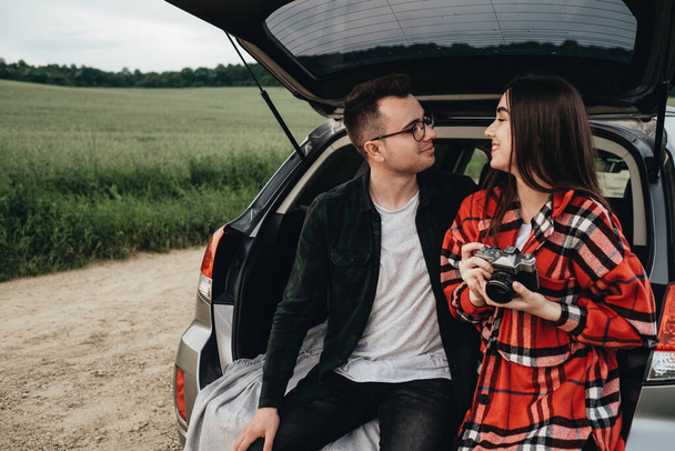 Młoda piękna para siedzi w bagażniku samochodowym i cieszy się z podróży - Zdjęcie, obraz