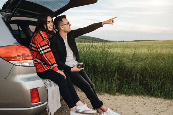 Młoda piękna para siedzi w bagażniku samochodowym i cieszy się z podróży - Zdjęcie, obraz