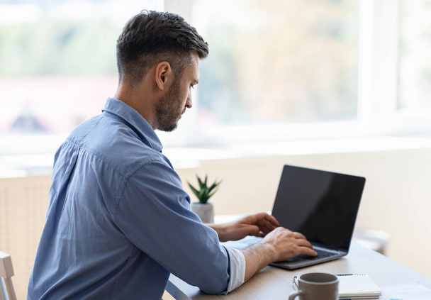 Drukke mannelijke ondernemer werken op laptop met zwart scherm in Office - Foto, afbeelding