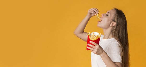 Giovane donna che mangia patate fritte francesi su sfondo giallo Studio - Foto, immagini