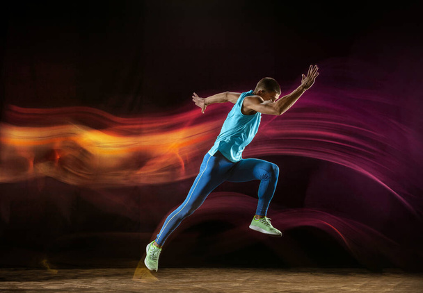 Professional male runner training isolated on black studio background in mixed light - Photo, Image