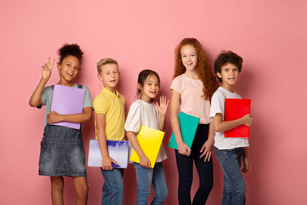 Portrét šťastných školních studentů s copybooks s úsměvem na růžovém pozadí - Fotografie, Obrázek