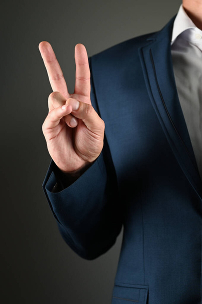 Az öltönyös férfi békejelképet mutat a kezével. Kiváló minőségű fénykép - Fotó, kép