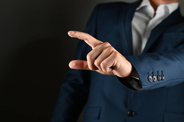 The man holds his index finger in front of him. A man in a suit points a finger forward on a black background. Concept: click on the button, specify specify. High quality photo - Foto, afbeelding