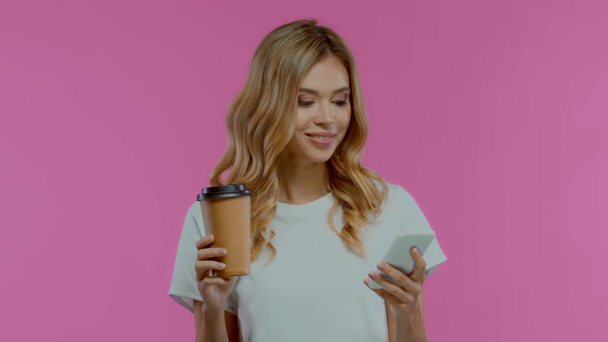 Jonge vrouw die koffie drinkt en toont smartphone geïsoleerd op paars - Video