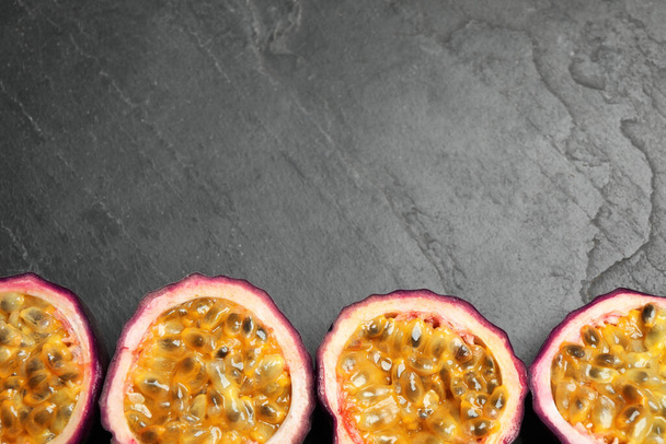 Halves of passion fruits (maracuyas) on black slate table, flat lay. Space for text - Фото, зображення