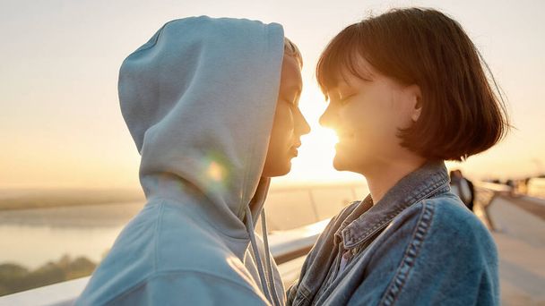 Lesbian couple hugging on the bridge, looking at each other before kiss while admiring the sunrise together - Photo, Image