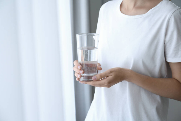 Mujer sosteniendo vaso de agua cerca de la ventana en casa, primer plano - Foto, imagen