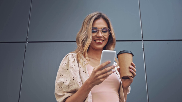 Mulher loira bebendo café e usando smartphone perto do edifício  - Filmagem, Vídeo
