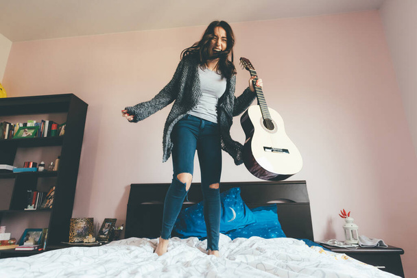 Onnellinen nuori nainen hyppää sänky kitara - Nainen taiteilija laulaa hyppy sänky innostunut - inspiraatiota, hauskaa, nauttia käsite - Valokuva, kuva