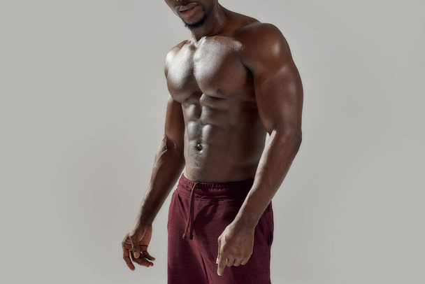 Rajattu laukaus lihaksikas afrikkalainen mies näyttää hänen alaston vartalo poseeratessaan paidaton eristetty yli harmaa tausta. Urheilu, harjoitus, kehonrakennus käsite - Valokuva, kuva