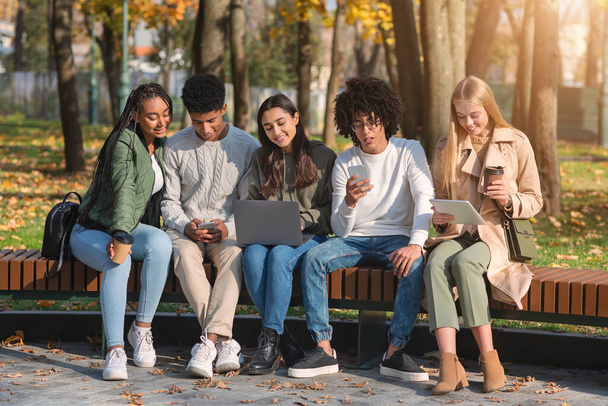 Εθισμένοι έφηβοι που χρησιμοποιούν gadgets ενώ περνούν χρόνο στο πάρκο - Φωτογραφία, εικόνα