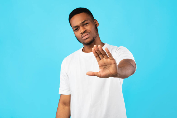 Serieuze zwarte man gebaren stoppen staande over blauwe achtergrond - Foto, afbeelding