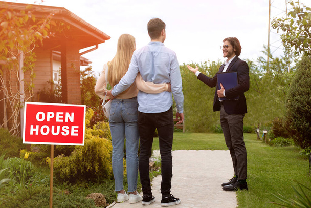 Confident real estate manager showing open house to young couple outside - Photo, Image