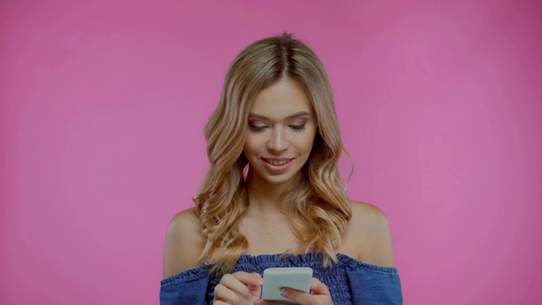 Blond vrouw met behulp van smartphone en kijken naar camera geïsoleerd op paars - Video