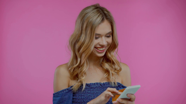 Blonde woman using smartphone and credit card isolated on purple - Felvétel, videó