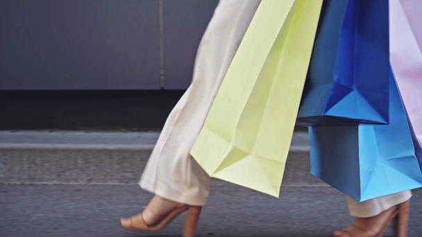 Vista recortada de la mujer sosteniendo bolsas de compras mientras camina por la calle - Imágenes, Vídeo