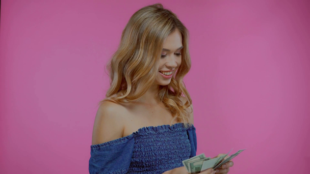 Blonde woman counting and throwing dollars isolated on purple - Filmmaterial, Video