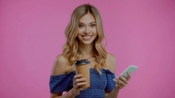 Mulher loira usando smartphone e segurando café para ir isolado em roxo - Filmagem, Vídeo