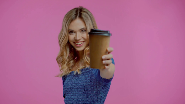 Mujer rubia bebiendo y mostrando café para ir aislado en púrpura - Imágenes, Vídeo
