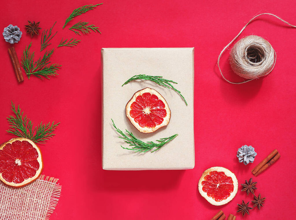 Minimalistic stylish bright Χριστουγεννιάτικη σύνθεση από κουτί δώρου σε χαρτί χειροτεχνίας σε κόκκινο φόντο.Η έννοια της μηδενικής σπατάλης.Οικολογική φυσική διακόσμηση για συσκευασία χριστουγεννιάτικων δώρων.. - Φωτογραφία, εικόνα