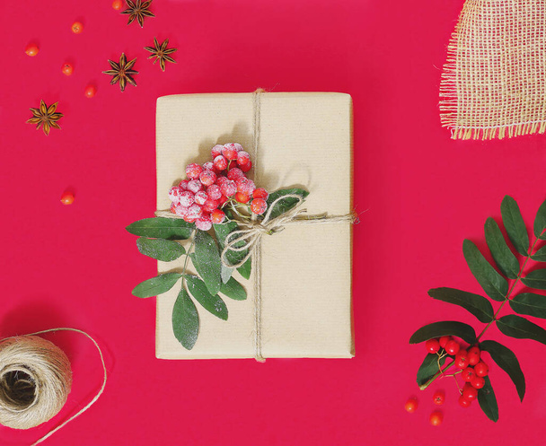 Minimalistische stilvolle helle Weihnachtskomposition aus einer Geschenkschachtel in Bastelpapier auf rotem Hintergrund. Das Konzept der Null-Verschwendung. Umweltfreundliches natürliches Dekor für die Verpackung von Weihnachtsgeschenken. Flache Lage. - Foto, Bild