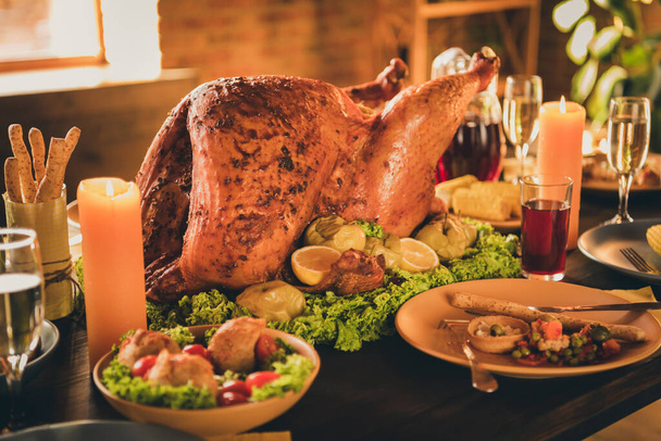 Closeup photo of big baked roast crisp stuffed turkey lettuce soaked apple decor garnish cutlery grissini red beverage glass dishes two lighted candles in living room indoors - 写真・画像