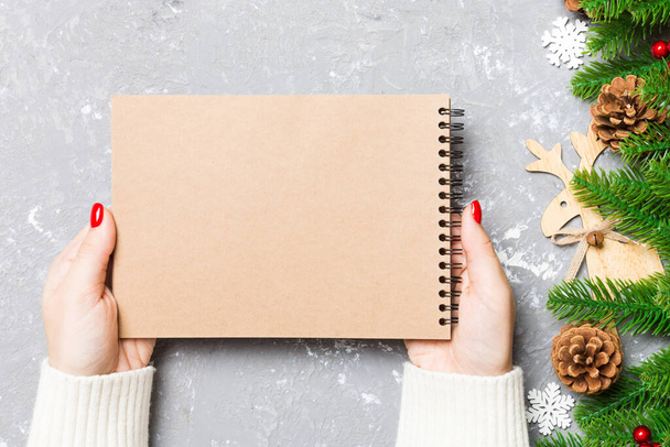 Top view of female hand holding a notebook on cement Christmas background. fir tree and festive decorations. Wish list. New Year concept. - Photo, Image