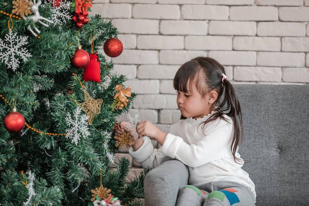 Ein nettes Kind schmückt den Weihnachtsbaum und hat Spaß. Fokus auf die Tochter - Foto, Bild