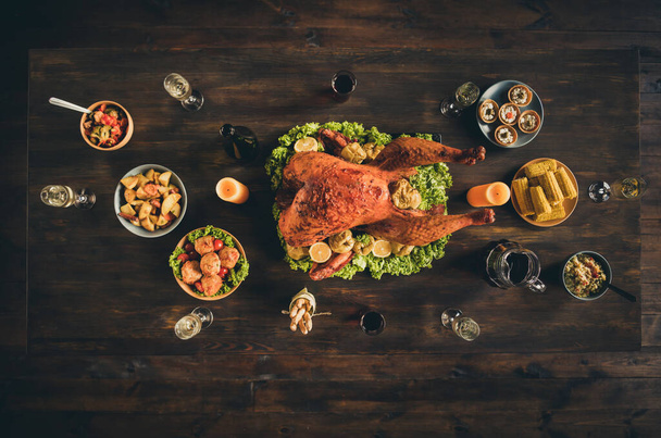 Top above high angle photo of big baked roast stuffed turkey garnish rice potato wine vegetable fruit salad decor family gathering two candles in living room without people indoors - Photo, image