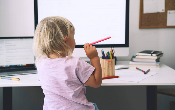 Little girl studying and drawing at desk. Preschool child using computer in early development or entertainment at home. Children homeschooling and distance online education. Kids online learning. - 写真・画像