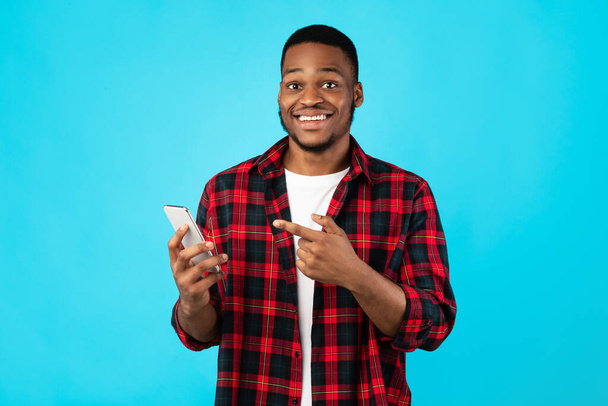 アフリカの男は青の背景の上に立ってスマートフォンで指を指す - 写真・画像