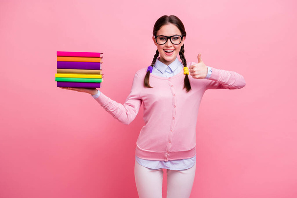 Photo of pretty student lady hold books pile diligent pupil prefer read literature rise thumb up approve interesting story wear shirt pullover pants specs isolated pink color background - Foto, Imagen