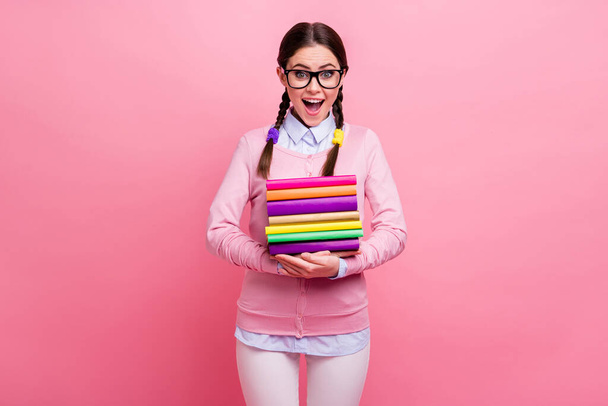 Photo of funny pretty girlish student lady two nice braids hold many books diligent pupil visit library dream reading wear shirt pullover pants specs isolated pastel pink color background - Фото, зображення