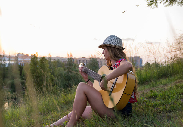 Sarışın kadın parkta oturmuş gitar çalıyor. - Fotoğraf, Görsel