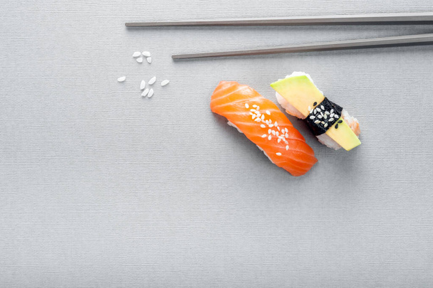 Nigiri sushi con salmón y aguacate sobre fondo gris con palillos, vista superior - Foto, Imagen
