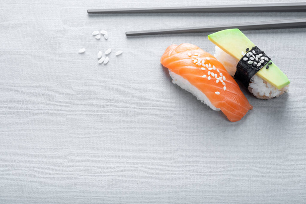 Nigiri sushi com salmão e abacate em um fundo cinza com pauzinhos, close-up - Foto, Imagem